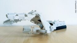 Image: The image shows a white 3D-printed hand exoskeleton placed on a wooden surface; Copyright: Fraunhofer IWU