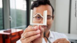 Image: The picture shows a researcher holding up a white structural model with a curved element; Copyright: University of Stuttgart 